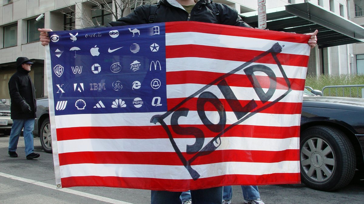 Title: Protestor holding Adbuster’s American corporate flag | Author: Jonathan McIntosh | Source: Wikimedia | License: CC BY 2.0